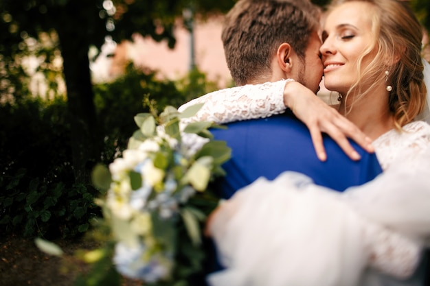 La mariée tient son voile sur sa main serrant le marié dans le parc