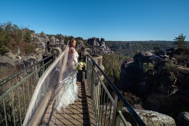 Une mariée vêtue d'une robe blanche avec un bouquet de fleurs sur fond de montagnes et de gorges en Saxe suisse, Allemagne, Bastei.