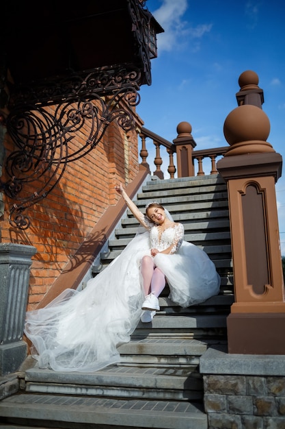 La mariée vêtue d'une robe de mariée blanche et de baskets blanches est assise sur les marches d'un grand bâtiment