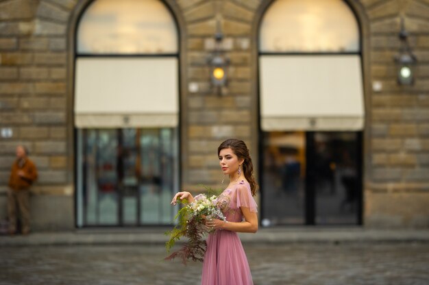 Une mariée vêtue d'une robe rose avec un bouquet se dresse au centre de la vieille ville de Florence en Italie