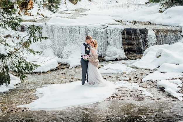 Les mariées posent en hiver sur fond de cascade gelée.