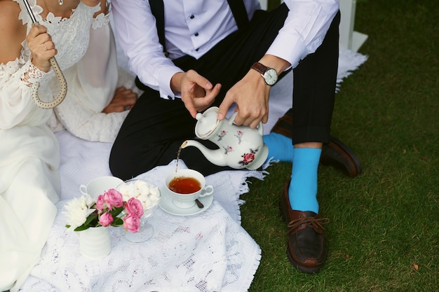 Les mariés boivent du thé dans des vêtements clairs sur l'herbe verte