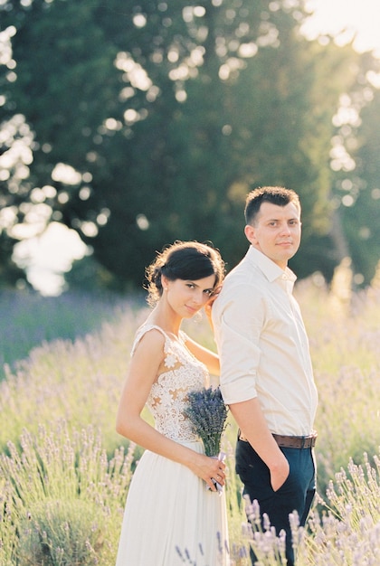 Les mariés avec un bouquet se tiennent sur un champ de lavande