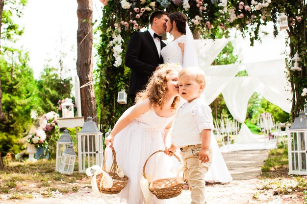 Les mariés s'embrassent après la cérémonie de mariage. Enfants adorables avec des pétales de rose volants dans des paniers