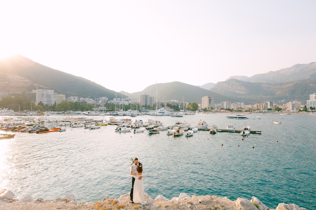 Les mariés s'embrassent et s'embrassent sur la plage dans le contexte de l'embarcadère de Budva.