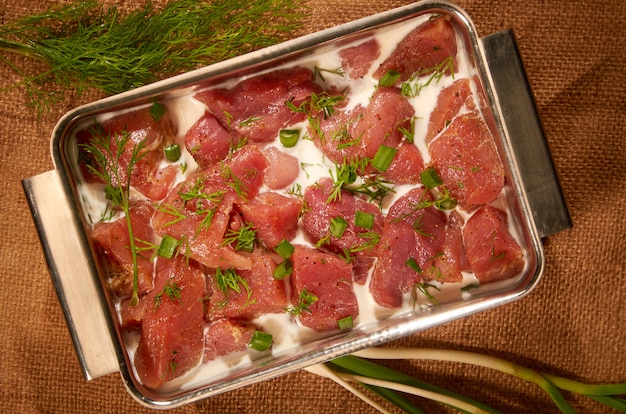 Mariné dans du lait et des herbes, la viande dans un pot en acier sur le tissu avec des herbes fraîches