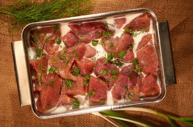 Mariné dans du lait et des herbes, la viande dans un pot en acier sur le tissu avec des herbes fraîches