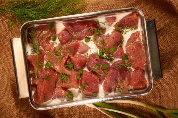 Mariné dans du lait et des herbes, la viande dans un pot en acier sur le tissu avec des herbes fraîches