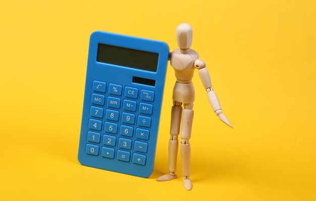 Marionnette en bois avec une calculatrice sur fond jaune. Coût, économie