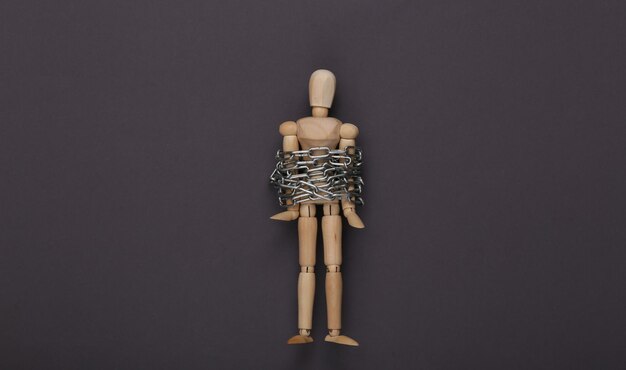 Marionnette en bois enveloppée dans une chaîne en acier sur fond gris Vue de dessus