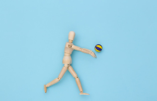 La marionnette en bois joue au volleyball avec la boule sur le fond bleu