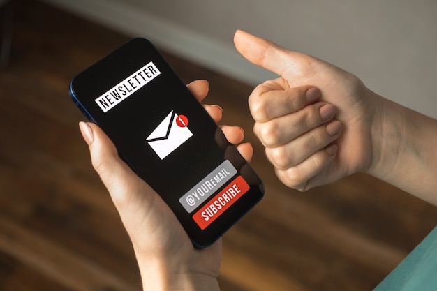 Marketing par e-mail et médias, communication avec fond de concept de newsletter. Téléphone portable avec page de newsletter d'inscription et clients satisfaits main dans le geste du pouce vers le haut à l'intérieur