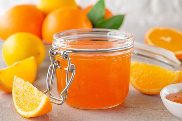 Marmelade d'orange ou confiture d'orange dans un bocal en verre avec des fruits frais sur fond gris Espace de copie