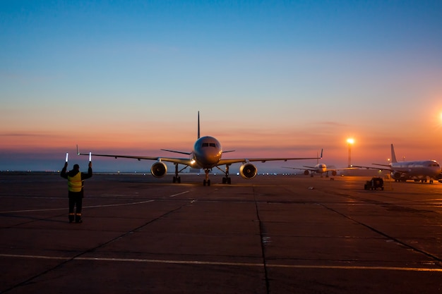 Le marshaller de l'aéroport rencontre l'avion à réaction qui roule jusqu'au parking sur le tablier de l'aéroport tôt le matin