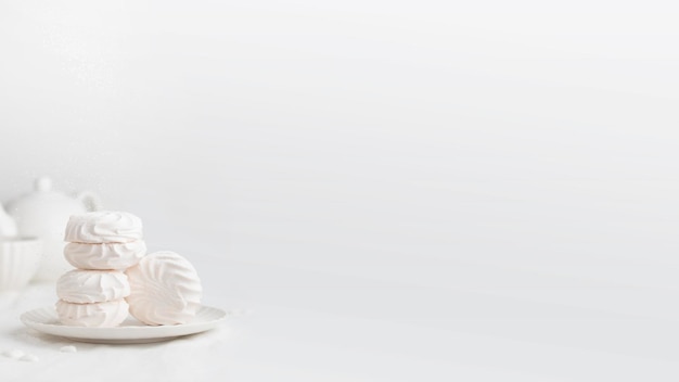 Photo marshmallows blancs moelleux ou coquilles de marshmallows avec des éclaboussures de sucre en poudre sur une assiette blanche sur une table blanche la bannière avec un espace de copie