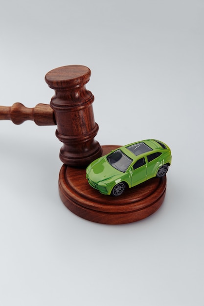 Marteau en bois du juge et petite voiture sur fond blanc. Assurance, affaire judiciaire. Image verticale.