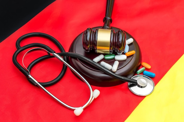 Photo marteau avec stéthoscope et pilules sur drapeau allemand droit médical