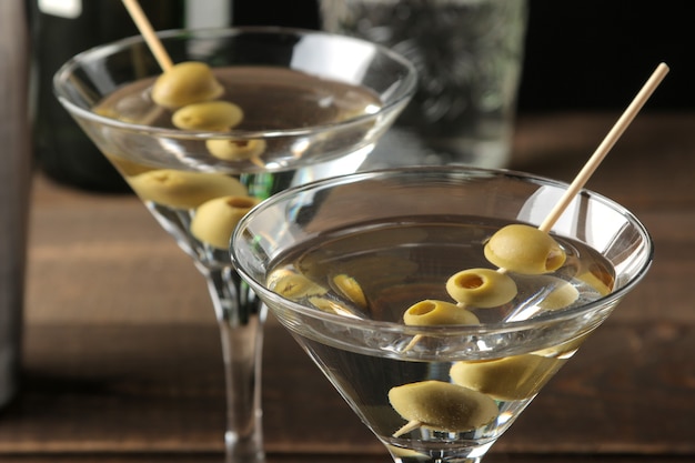 Martini dans un verre à vin en verre avec des olives vertes sur une brochette sur une table en bois marron. cocktails. bar