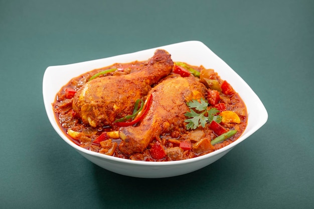 Masala de poulet indien, sauce épaisse au poulet épicé indien garnie de feuille de coriandre, piment rouge et vert qui est disposé dans un bol de service en céramique blanche sur fond vert, isolé.