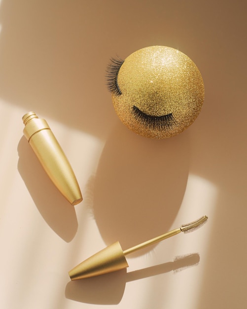 Mascara et une boule de Noël dorée avec de faux cils Le concept de maquillage festif pour les femmes