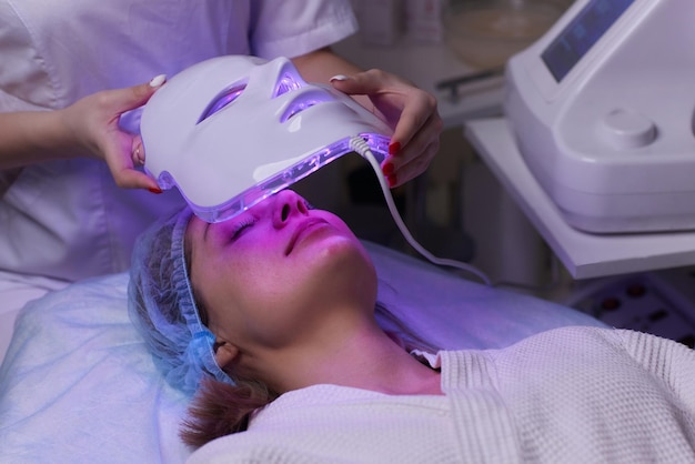 Masque anti-âge à lumière LED pour les soins de la peau du visage dans un spa au ralenti Une femme allongée sur un canapé dans un masque spécial Technologies modernes de beauté et de santé