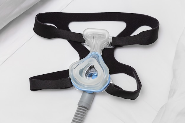 Masque CPAP, sangle du harnais et tuyau d&#39;air sur le lit blanc