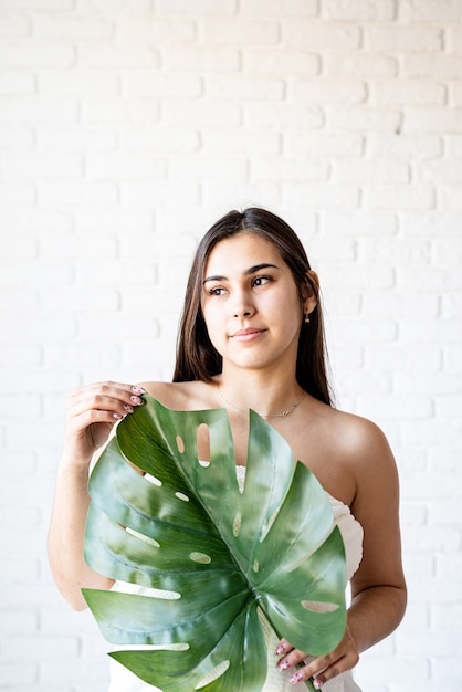 Masque facial de spa. Spa et beauté. Heureuse belle femme brune portant des serviettes de bain tenant une feuille de monstera verte devant son visage