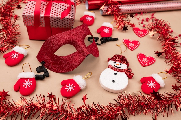 Un masque de mascarade brillant au centre, entouré de cadeaux, de guirlandes, d'un bonhomme de neige, de petites mitaines rouges et de rouleaux d'emballages cadeaux. . Le bonheur et la joie. Décorations pour la fête.