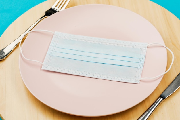 Masque médical sur une assiette vide avec une fourchette et un couteau sur un plateau en bois Le concept de nutrition et de protection contre le virus