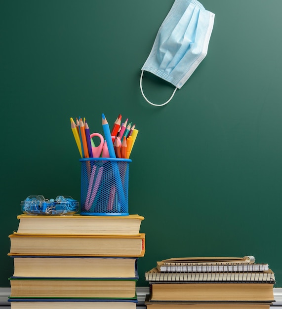 Masque médical jetable fournitures scolaires sur tableau de craie vert fond quarantaine scolaire