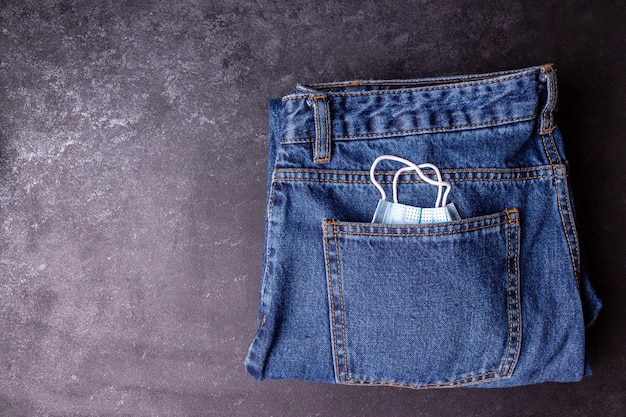 Un masque médical sort d'une poche de jeans sur fond noir, espace de copie