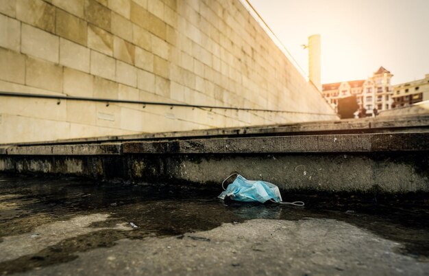 Masque médical usagé jeté au sol sur un bâtiment flou dans la ville Élimination des déchets médicaux