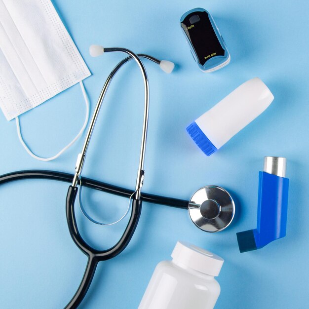 Photo masque médicale blanche stéthoscope oxymètre bouteille de pilules et d'inhalateurs sur fond bleu vue supérieure