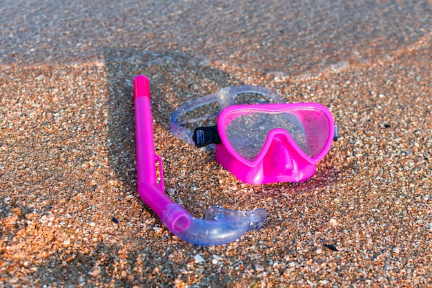 Le masque de natation rose et le tuba de plongée se trouvent sur le sable près de l'eau