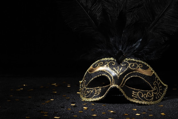 Photo masque d'or de carnaval avec des plumes et des confettis sur fond noir