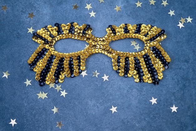 Photo masque scintillant d'or avec des étoiles dorées sur un mur bleu. vue de dessus, copiez l'espace.