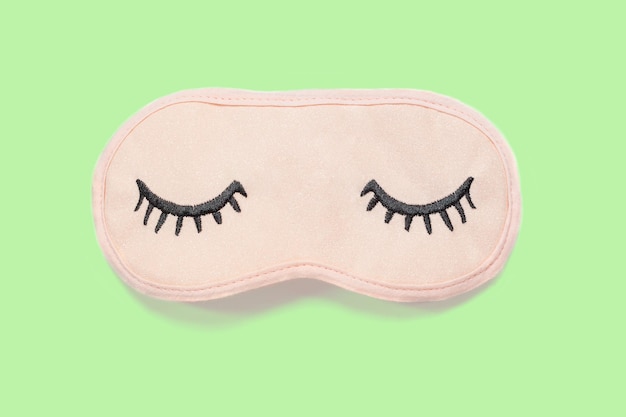 Photo masque de sommeil rose pastel avec des yeux fermés brodés avec des cils sur un fond vert pastel