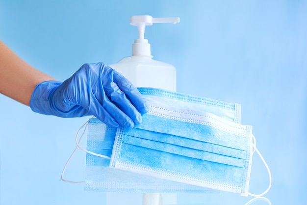 Masques médicaux, masque protecteur jetable chirurgical dans la main du médecin avec des gants bleus. Gel désinfectant pour alcool en bouteille. Coronavirus covid 19 hygiène de prévention des virus sur fond bleu.