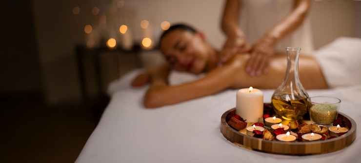Photo massage en aromathérapie dans un plateau de spa de luxe avec des bougies et de l'huile au premier plan et une jeune femme européenne