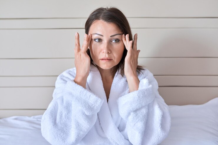Massage du visage anti-âge belle femme mature en peignoir blanc faisant un massage du visage assis à la maison au lit