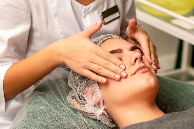 Massage du visage Belle jeune femme blanche caucasienne ayant un massage facial avec les yeux fermés dans un salon de spa