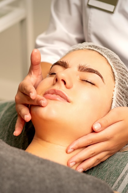 Massage du visage Belle jeune femme blanche caucasienne ayant un massage facial avec les yeux fermés dans un salon de spa