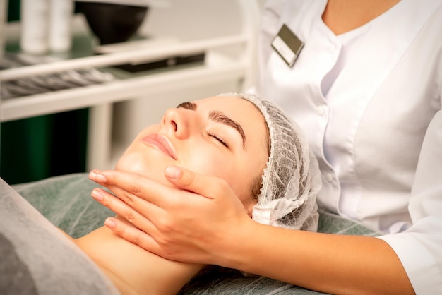 Massage du visage Mains d'un masseur massant le cou d'une jeune femme caucasienne dans un salon de spa le concept de massage de santé