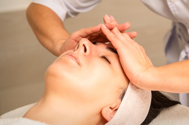 Massage facial Jeune femme caucasienne aux yeux fermés se faisant masser le front dans un salon de beauté