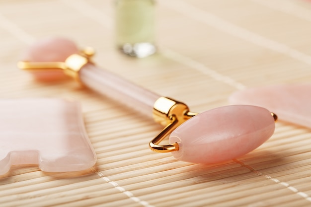 Massage Gua sha à base de Quartz rose naturel, pierre de jade et huile, sur fond de bambou pour les soins du visage et du corps.