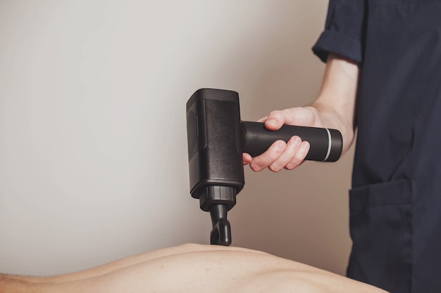 Massage de percussion de pistolet de sport dans la salle médicale du gymnase. Masseur fait des exercices de massage à domicile. Thérapie par percussions pour le massage régénérant du corps sportif. Concepts de réhabilitation des blessures. Espace de copie