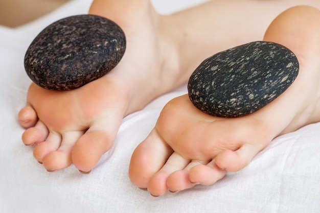 Massage des pieds sur les jambes de la femme par des pierres chaudes se bouchent.