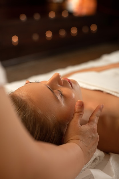 Massage relaxant. Une femme séduisante et impeccable aux cheveux attachés dormant pendant un massage du visage dans un centre SPA professionnel