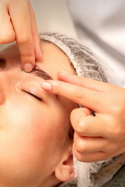 Massage des sourcils Belle jeune femme blanche caucasienne recevant un massage des yeux et des sourcils avec les yeux fermés dans un salon de spa