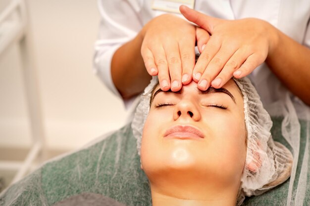 Massage de la tête Belle jeune femme blanche caucasienne recevant un massage de la tête et du front avec les yeux fermés dans un salon de spa